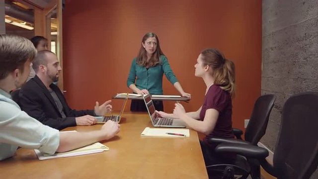 Woman leading a small business meeting when an intern brings her a note and she leaves
