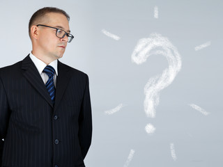 Businessman is thinking and looking at chalk drawn question mark over gray background
