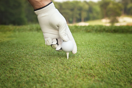 Selective focus of golfer's hand placing ball on tee