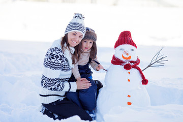 Happy beautiful family building snowman in garden, winter, mom a
