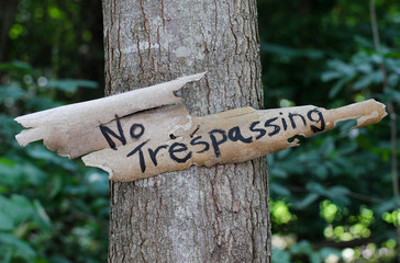 Weathered No Trespassing sign hanging on tree