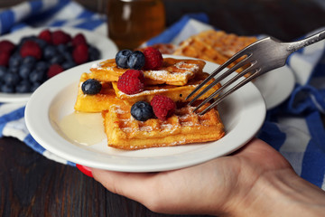Woman eating Sweet homemade waffles with forest berries and sauce, close-up