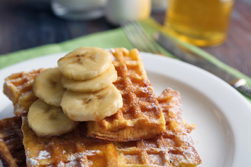 Sweet homemade waffles with sliced banana on plate, on light background