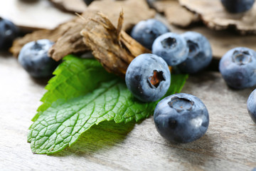 Tasty ripe blueberries with green leaves on wooden table close up