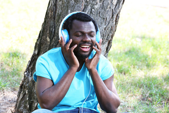 African American man with headphones near tree in park