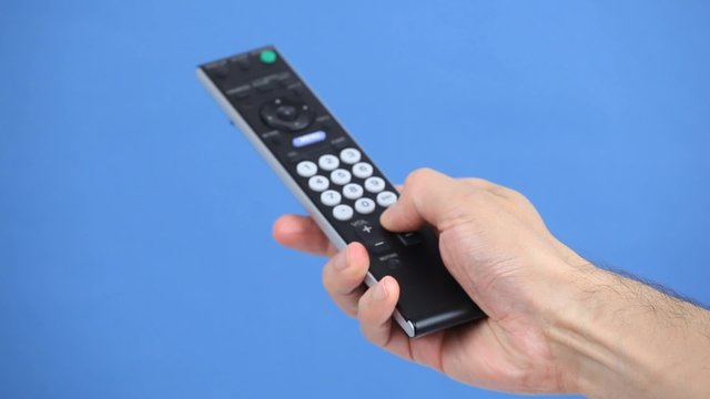 Close up of a remote control in hand on blue background