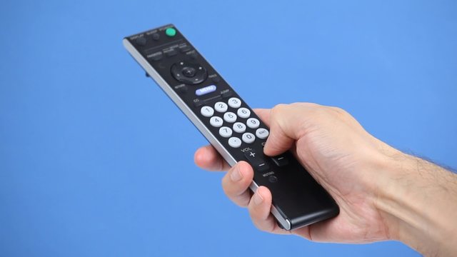 Close up of a remote control in hand on blue background
