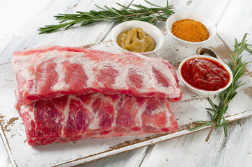 Raw ribs with sauces on a cutting board.
