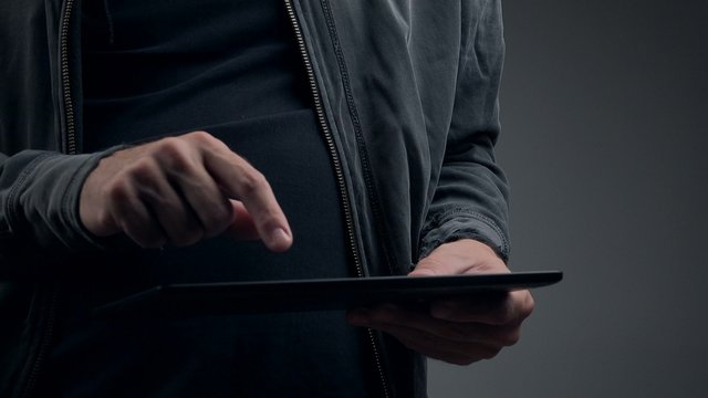 Cyber criminal with digital tablet computer trying to hack password for internet web page account, p2p and piracy concept.