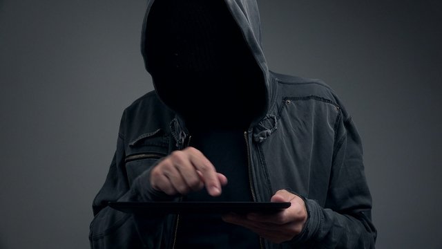 Hooded cyber criminal using digital tablet computer to access deep web internet page, p2p, piracy or network security concept, 4k uhd footage