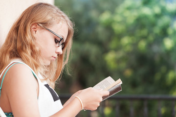 Blond teenage girl on the balcony with book