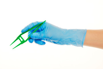 Close up of female doctor's hand in blue sterilized surgical glove with green plastic forceps against white background