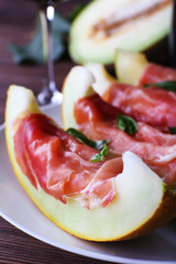 Melon with prosciutto of Parma ham on wooden table, closeup