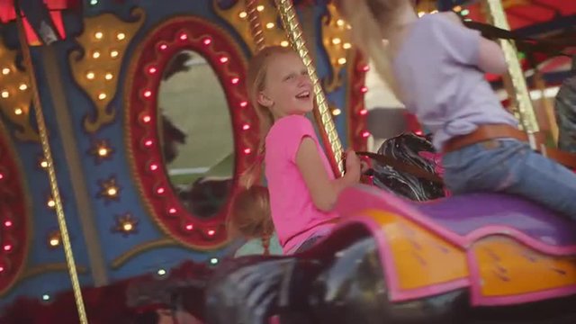 Three girls riding on a carousel and laughing together
