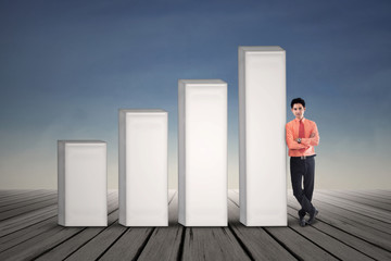 Fototapeta premium Young businessman standing next to growing bar chart