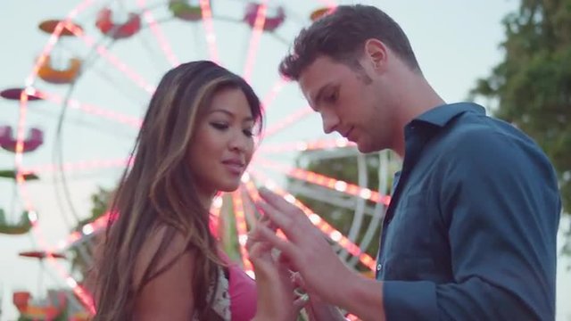 A couple looking at the camera and being romantic in front of a ferris wheel
