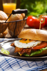 Sandwich with a fried egg, bacon, cheese and vegetables.