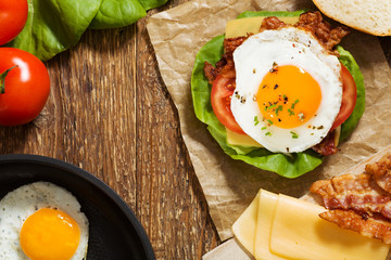 Sandwich with a fried egg, bacon, cheese and vegetables.