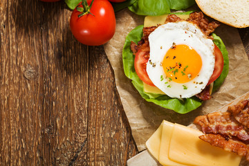 Sandwich with a fried egg, bacon, cheese and vegetables.