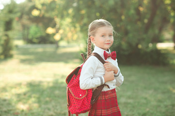 Happy kid girl 6-8 year old wearing school uniform outdoors. Looking at camera. Back to school. Childhood. 