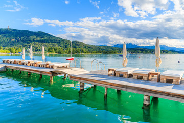 Sunchairs on wooden pier and view of beautiful alpine lake Worthersee in summer, Austria