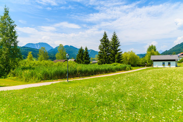 Rural walking path along green meadow in summer landscape of Alps Mountains, Weissensee lake, Austria