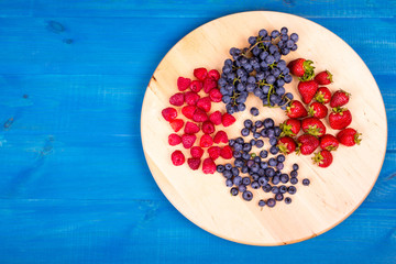 Strawberries, raspberries,  blueberries and grapes on wooden plate