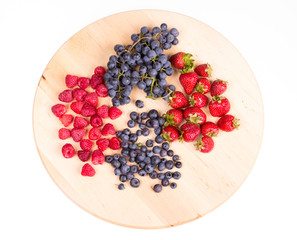 Strawberries, raspberries,  blueberries and grapes on wooden plate