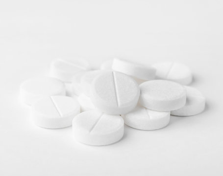 A heap of white medicine pills on white surface.