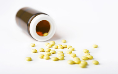 Yellow spilled Pills from a bottle on white surface