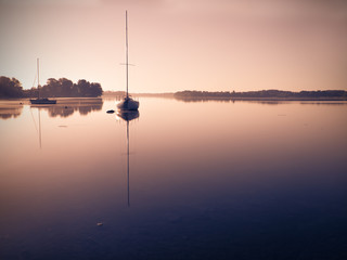 Little sailing boats reflect in  the serene water during sunrise.