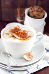 Figs in yogurt and honey in white porcelain cup on brown background.