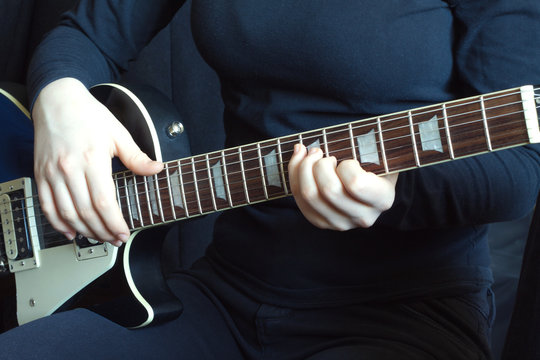 Musician in black on a black six strings electric guitar playing. Hands of the musician close up