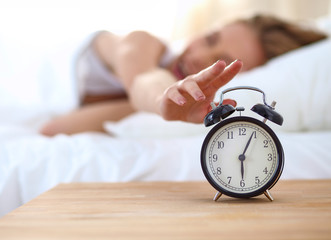 Young sleeping woman and alarm clock in bedroom at home