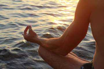 Close up on male hands meditating in yoga position on the beach near the sea at sunset
