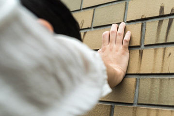 汚れた壁に手をついてうなだれる女性