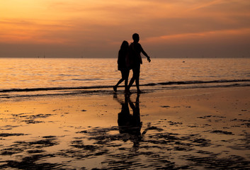 Silhouete of couple walking on the beach at sunset 