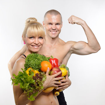 Attractive happy middle-age fit man and woman holding fruit and
