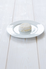 Camembert round entirely  on a white plate and a white wooden background