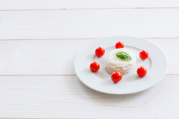 Camembert round entirely with cherry tomatoes and basil leaf on a white plate and a white wooden background