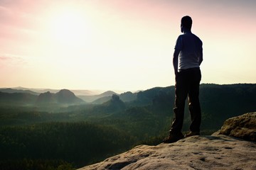 Satisfy tall hiker in grey shirt and dark trousers. Sprtsman on the peak of sharp rock edge ...