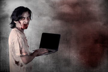 Scary male zombie typing with laptop