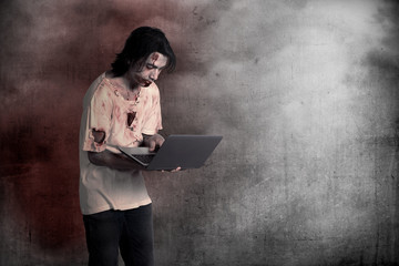 Scary male zombie typing with laptop