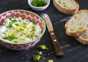 ricotta cheese with olive oil, herbs and pistachios - tasty Breakfast or snack, in a bowl on a dark wooden surface