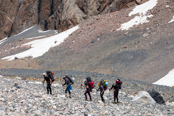 People traveling in mountains Large group of tourists of different sex ethnic nation race age young and old man woman walking up on difficult wild rocky terrain Steep Mountain Landscape in Background