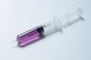 syringe with purple liquid on light background