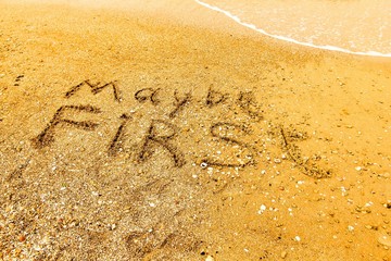 The word MAYBE FIRST written on a sandy beach in bold.