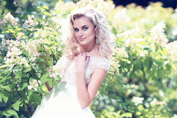 Beautiful bride posing outdoor. Wedding dress, curly blond hair.