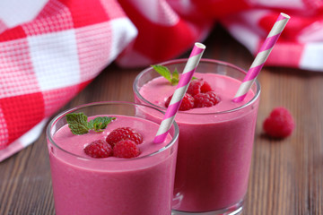 Glasses of raspberry milk shake with berries on wooden table close up