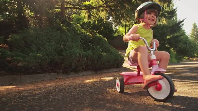 An adorable little girl happily riding her tricycle
